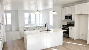 Kitchen with white cabinetry, appliances with stainless steel finishes, an island with sink, decorative light fixtures, and light wood-type flooring (pictures of home previously built)
