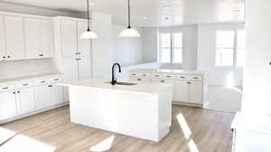 Kitchen featuring an island with sink, white cabinets, hanging light fixtures, light wood-style floors, and recessed lighting (pictures of home previously built)