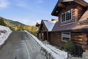View of snow covered exterior with log siding, a mountain view, and roof with shingles