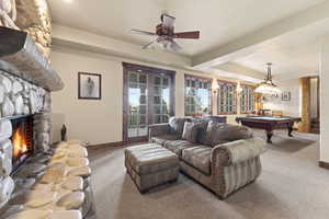 Living area featuring a raised ceiling, billiards table, carpet floors, french doors, and a stone fireplace