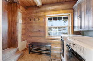 Laundry area featuring rustic walls, separate washer and dryer, and a wooden ceiling with exposed beams