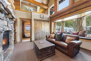 Carpeted living area featuring a fireplace, high vaulted ceiling, and a wood ceiling with exposed beams