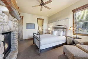 Bedroom with a stone fireplace, carpet floors, a ceiling fan, and ensuite bath