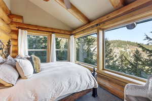 Carpeted bedroom with lofted ceiling and log walls