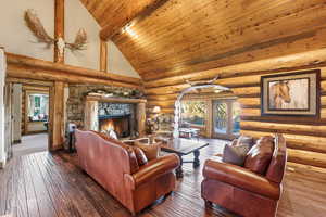 Living room featuring wood ceiling, high vaulted ceiling, rustic walls, hardwood / wood-style flooring, and a stone fireplace