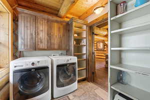 Laundry room featuring log walls, stone floors, wood ceiling, and washer and dryer
