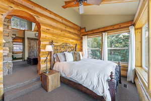 Carpeted bedroom with arched walkways, a ceiling fan, high vaulted ceiling, and log walls