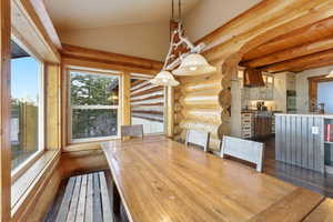 Unfurnished dining area featuring log walls, dark wood-type flooring, and vaulted ceiling