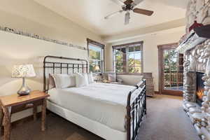 Carpeted bedroom with a stone fireplace, access to outside, and a ceiling fan