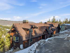 Snow covered property with log exterior, a garage, and a chimney