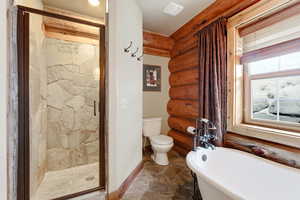 Bathroom with a shower stall, a freestanding bath, dark stone finish flooring, and rustic walls