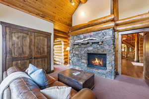 Carpeted living area with rustic walls, a stone fireplace, wood ceiling, high vaulted ceiling, and stairway
