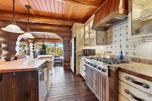 Kitchen featuring decorative light fixtures, premium range hood, log walls, dark wood-style floors, and stainless steel appliances