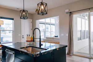 Kitchen with dark cabinetry, a center island with sink, hanging light fixtures, and dark stone counters