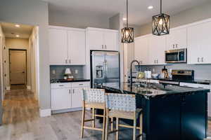 Kitchen featuring backsplash, stainless steel appliances, decorative light fixtures, recessed lighting, and a center island with sink