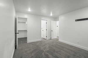 Unfurnished bedroom featuring a walk in closet and dark carpet