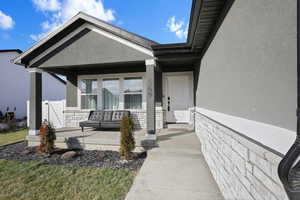 View of exterior entry featuring stone siding, stucco siding, covered porch, and a gate