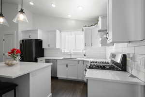 Kitchen featuring light stone countertops, stainless steel appliances, a kitchen bar, white cabinetry, and vaulted ceiling