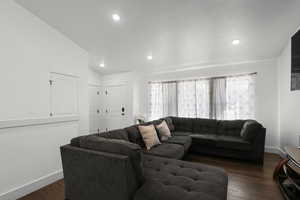Living room featuring dark wood-type flooring, vaulted ceiling, and recessed lighting