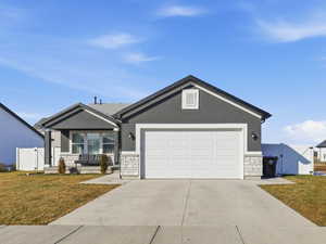Ranch-style house featuring stone siding, a gate, concrete driveway, and an attached garage