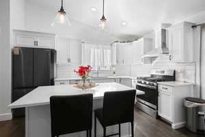 Kitchen featuring gas range, vaulted ceiling, white cabinets, wall chimney range hood, and a center island