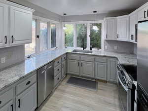 Kitchen featuring light stone counters, appliances with stainless steel finishes, decorative backsplash, and decorative light fixtures