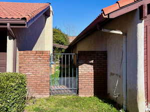 View of side of property featuring brick siding, a gate, and stucco siding