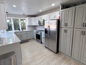 Kitchen with appliances with stainless steel finishes, light stone countertops, pendant lighting, gray cabinets, and light wood-style floors