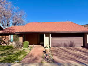 Ranch-style home with concrete driveway, a garage, brick siding, a tiled roof, and a front lawn