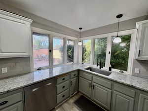 Kitchen featuring light stone counters, dishwasher, decorative light fixtures, light wood-style flooring, and decorative backsplash
