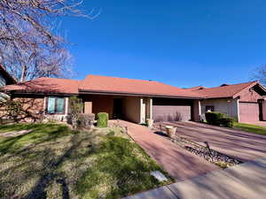 Ranch-style home with driveway, a front yard, a tile roof, an attached garage, and stucco siding