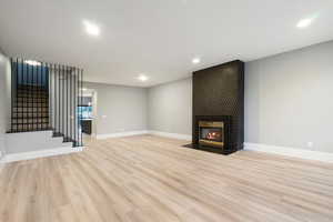 Unfurnished living room with a tile fireplace, light wood-type flooring, stairs, and recessed lighting