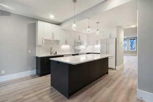 Kitchen with white cabinets, dark cabinets, a center island, white appliances, and hanging light fixtures