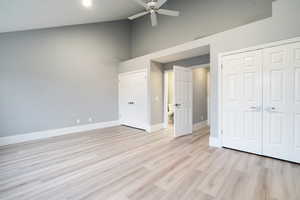 Unfurnished bedroom with high vaulted ceiling, light wood finished floors, a ceiling fan, and two closets
