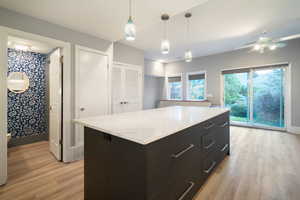 Kitchen featuring dark cabinets, pendant lighting, a center island, light wood-type flooring, and light stone countertops
