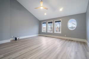 Empty room with high vaulted ceiling, light wood-style floors, and a ceiling fan