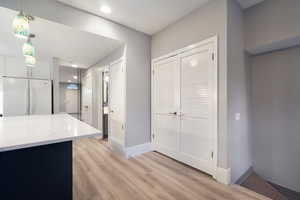 Kitchen featuring decorative light fixtures, white fridge, light stone countertops, light wood-style flooring, and recessed lighting