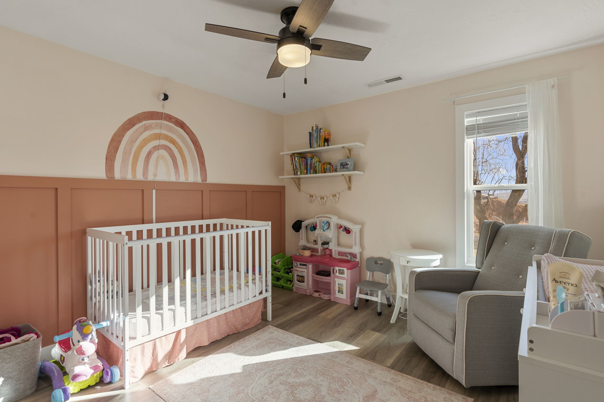 Bedroom featuring a crib, wood finished floors, ceiling fan, and a decorative wall