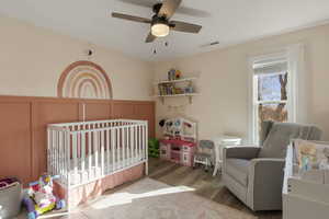Bedroom featuring a crib, wood finished floors, ceiling fan, and a decorative wall