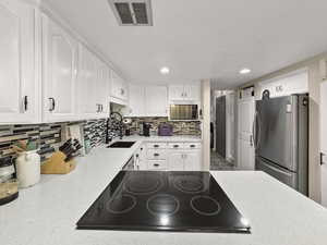 Kitchen featuring black electric stovetop, freestanding refrigerator, white cabinets, recessed lighting, and a textured ceiling
