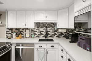 Kitchen with white cabinetry, stainless steel appliances, light stone counters, and tasteful backsplash