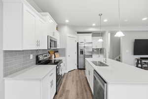 Kitchen with stainless steel appliances, decorative backsplash, hanging light fixtures, white cabinets, and an island with sink