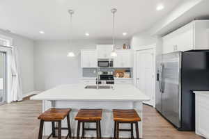 Kitchen featuring appliances with stainless steel finishes, a kitchen breakfast bar, decorative light fixtures, light wood-type flooring, and a center island with sink