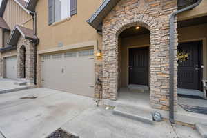 View of exterior entry with stone siding, stucco siding, concrete driveway, and a garage