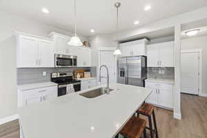 Kitchen with stainless steel appliances, a breakfast bar area, pendant lighting, light wood-style flooring, and white cabinets