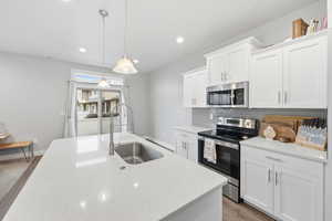 Kitchen featuring appliances with stainless steel finishes, hanging light fixtures, white cabinetry, light stone counters, and recessed lighting