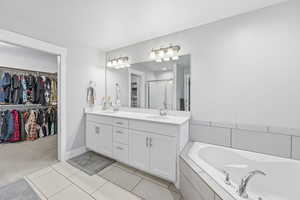 Full bathroom featuring a walk in closet, double vanity, a stall shower, a bath, and light tile patterned flooring