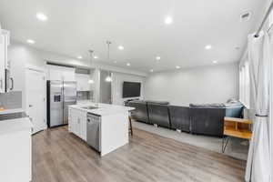 Kitchen featuring open floor plan, decorative light fixtures, tasteful backsplash, stainless steel appliances, and white cabinetry
