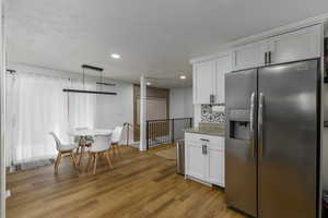 Kitchen with stainless steel refrigerator with ice dispenser, white cabinetry, light stone countertops, light wood-type flooring, and recessed lighting