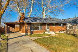 Ranch-style house featuring an attached carport, a chimney, concrete driveway, brick siding, and roof with shingles